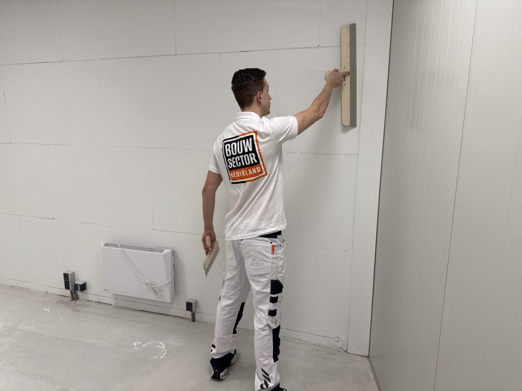 Stukadoor met het logo van Bouwsector Nederland op zijn rug trekt een nieuwe binnenwand vlak met een lange spaan